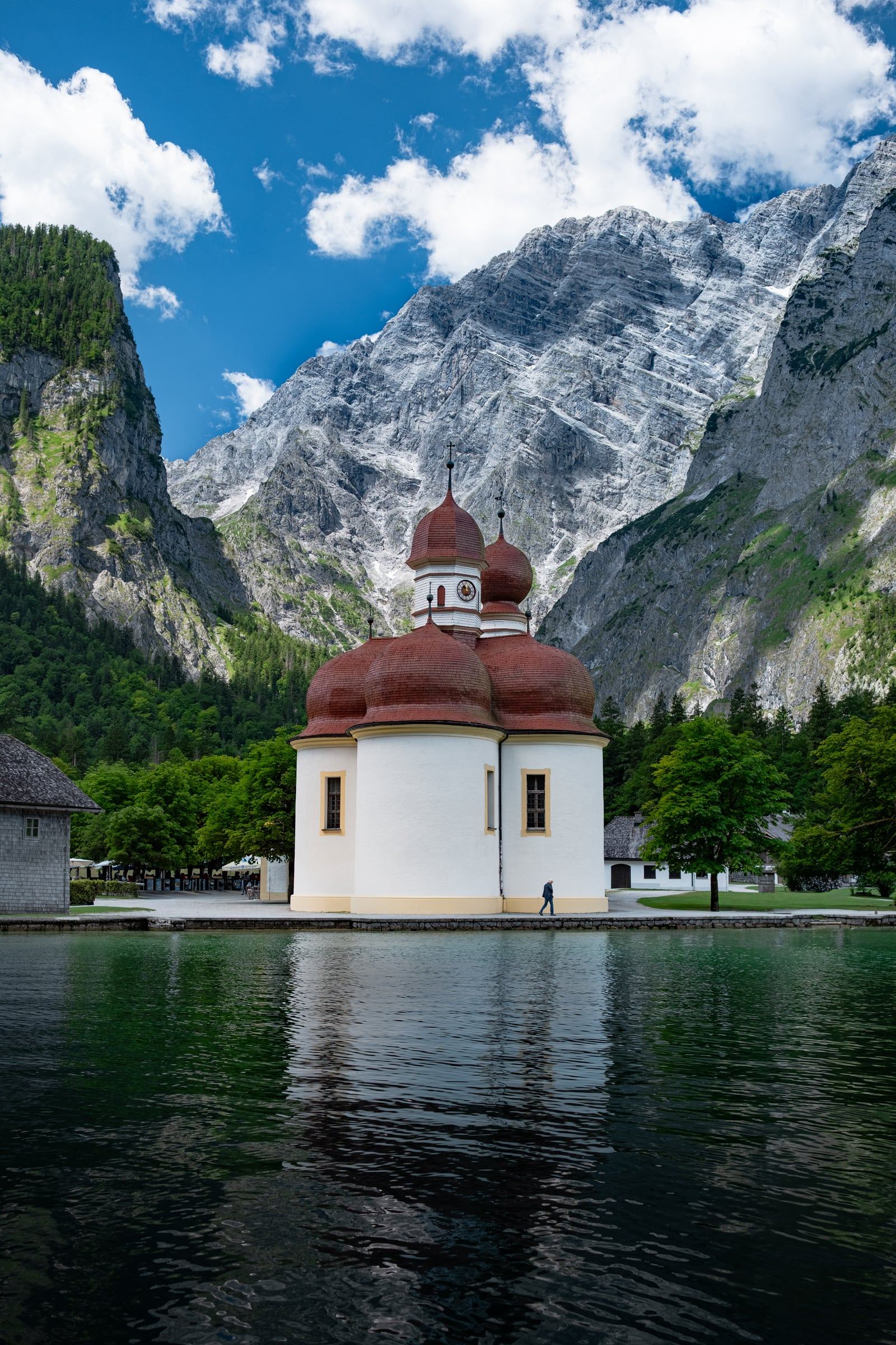 The red-domed chapel of St. Bartholomä on the shore of a green lake under towering cliffs.
